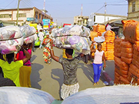 young boy walking on a crowded city street with a very large cloth package balanced on his head